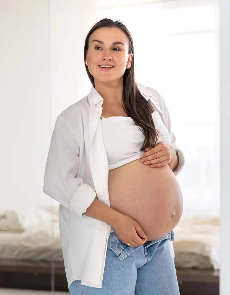Mulher grávida sorrindo, com a mão na barriga