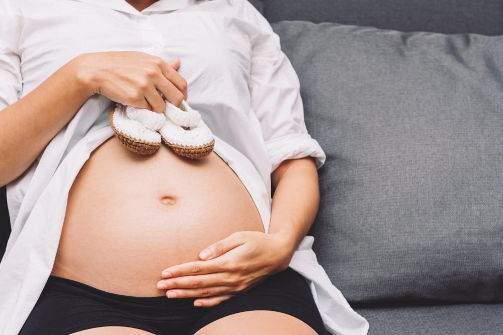 Gestante segurando sapatinhos de bebê sobre a barriga