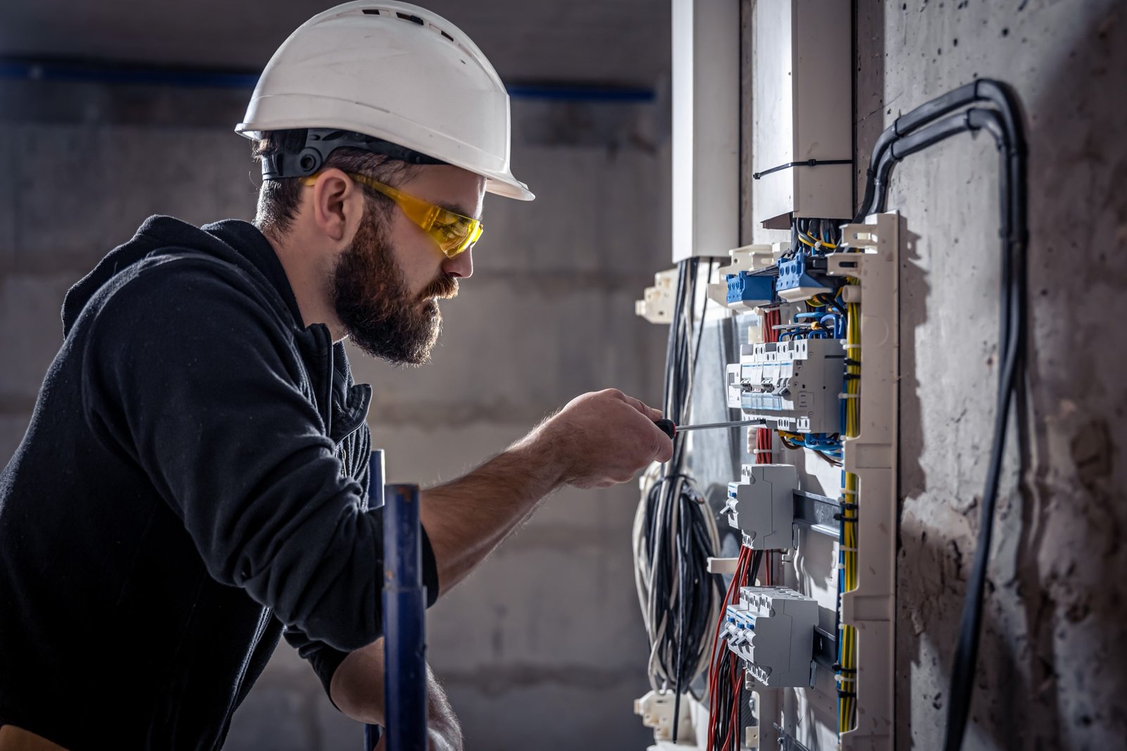 Eletricista com capacete e óculos de proteção trabalhando em um quadro de energia