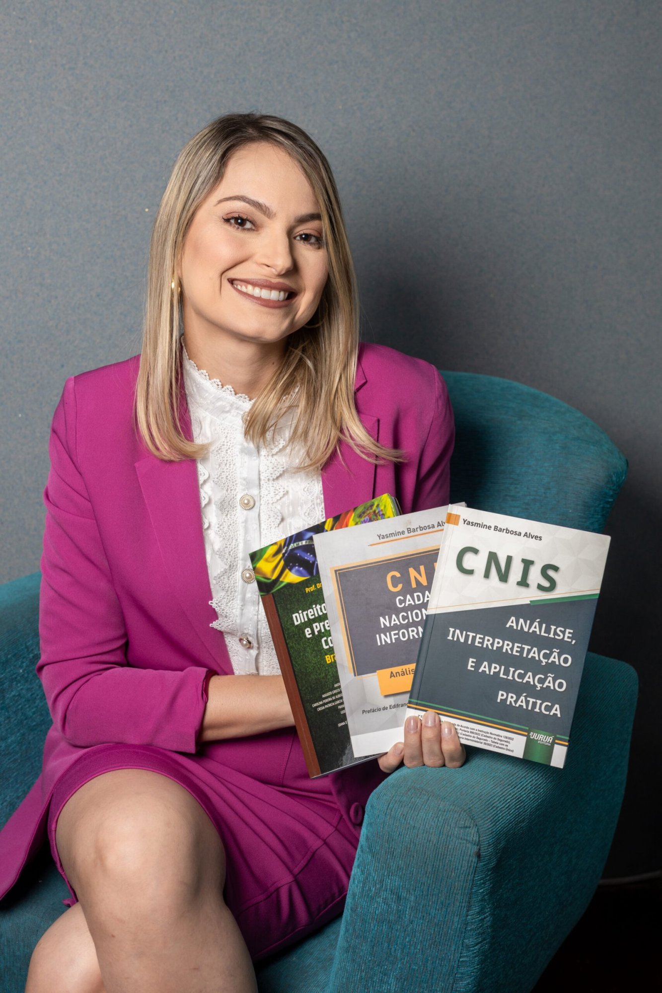 Dra. Yasmine Barbosa Alves sentada em uma poltrona e segurando livros jurídicos sobre CNIS