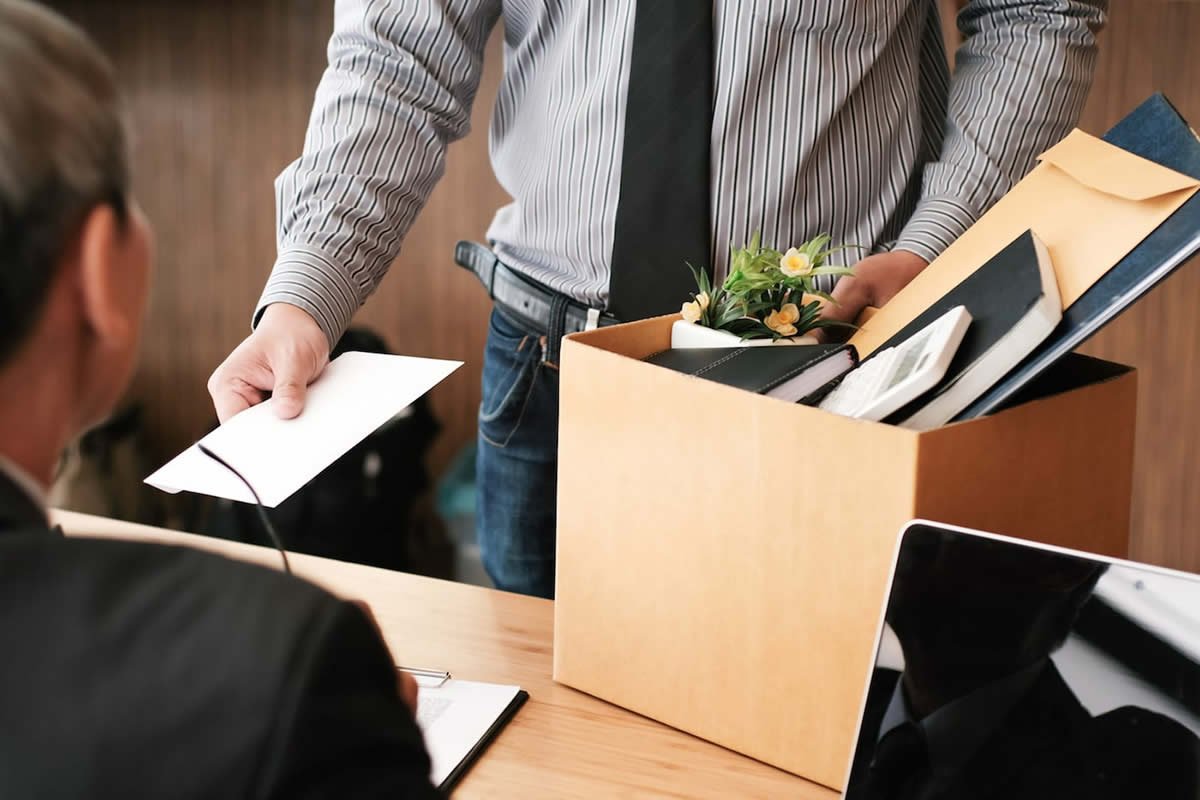 Funcionário com caixa de pertences entregando uma carta de desligamento