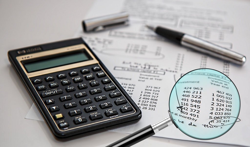 Calculadora, caneta e lupa sobre planilha de valores